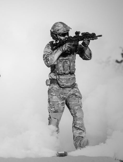 Black and white image of soldiers in a tactical operation amidst smoke and sand.